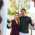Excited,Couple,At,Entrance,Door,With,Bottle,Of,Wine.,Friends